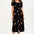 A model wearing a midi dress with a square neckline, short sleeves, and a shirred bust. The dress has a black background with a vibrant Tropical Parrots print in colorful patterns.