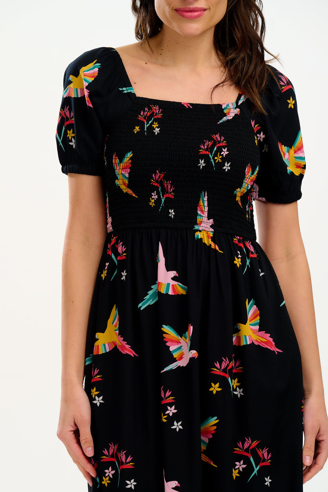 Black dress with colorful parrot and flower patterns worn by a model on a white background