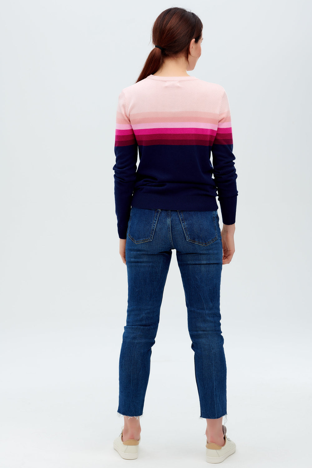 Sugarhill Brighton model wearing a navy jumper with pink gradient stripes, paired with jeans, standing against a white background.