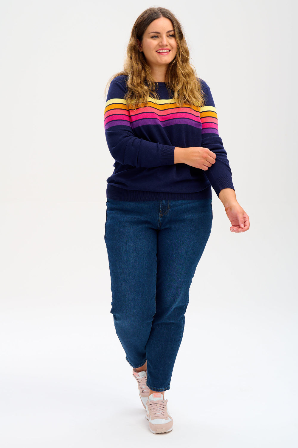 Sugarhill Brighton model wearing a navy blue jumper with horizontal retro stripe bands in pink, yellow, and other colours across the chest and shoulders.