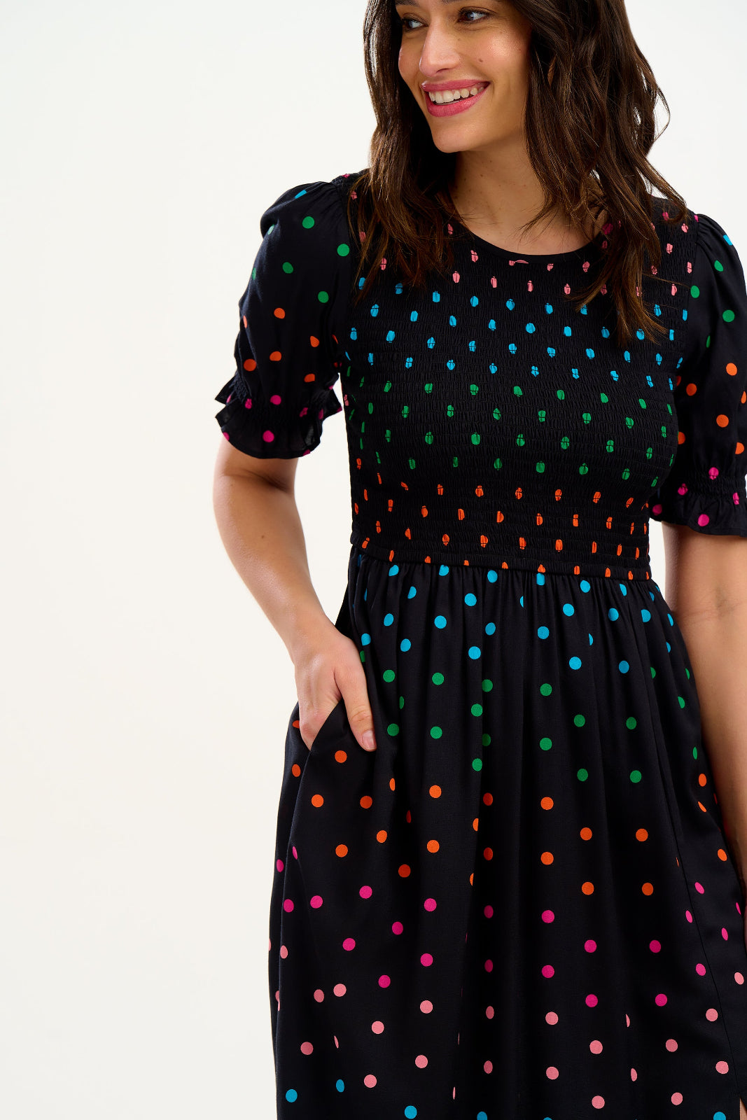 A model wearing a midi shirred dress with a black and rainbow polka print. The dress features a shirred bodice, elasticated puff sleeves, and a split hem.