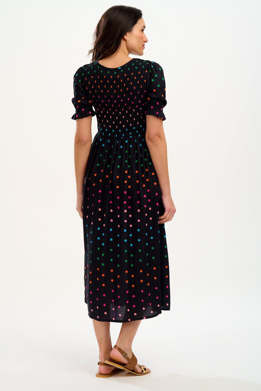 A model wearing a midi shirred dress with a black and rainbow polka print. The dress features a shirred bodice, elasticated puff sleeves, and a split hem.
